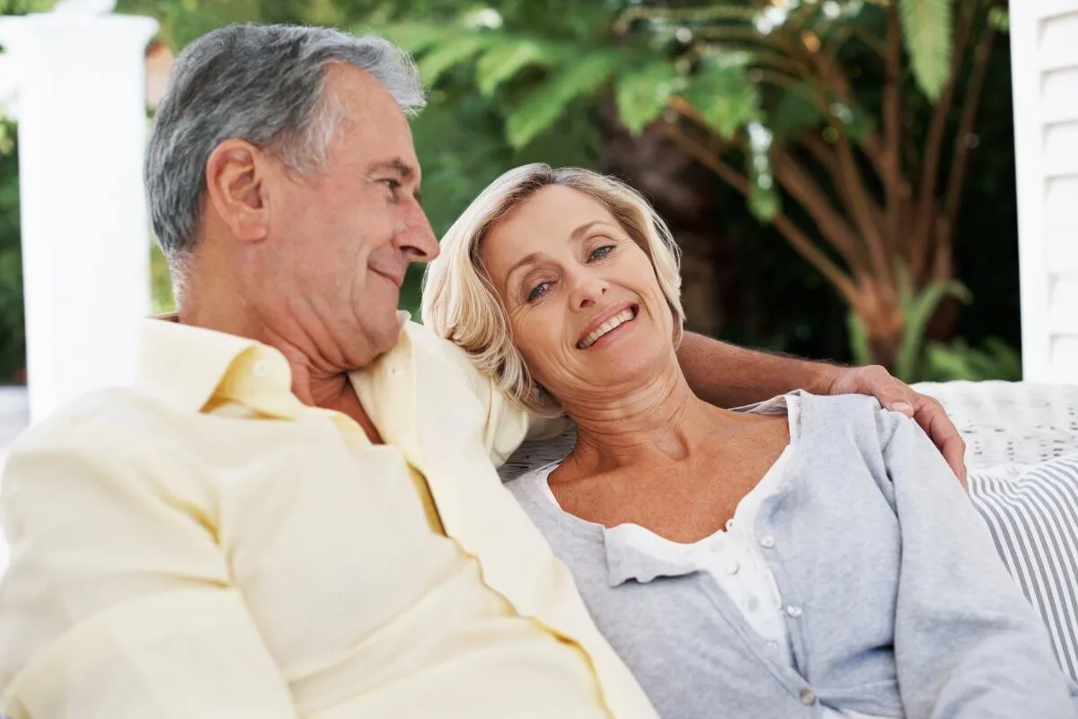 An older man looking at his wife adoringly while she smiles at the camera.