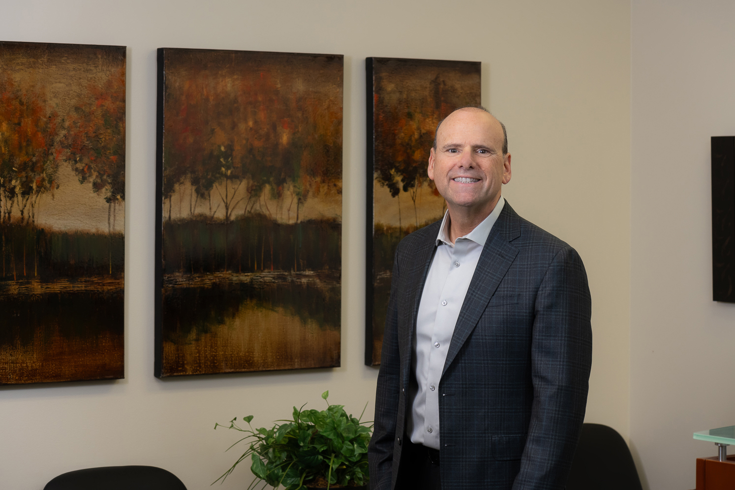 user-inserted A man in a suit stands confidently in front of several colorful paintings in an art gallery setting.